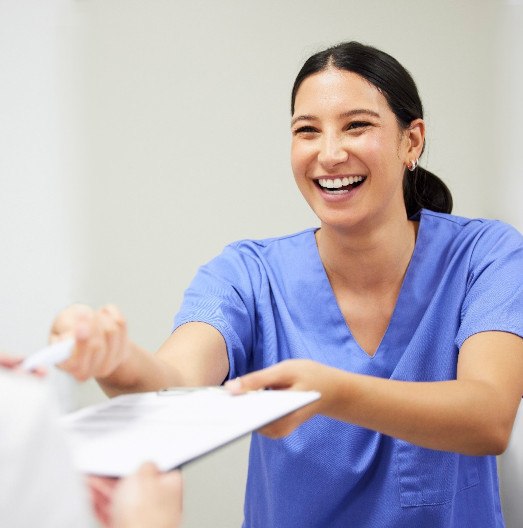 Dental assistant smiling while handing patient form