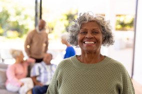 Woman in a green sweater smiling with a blurry social gathering in the background