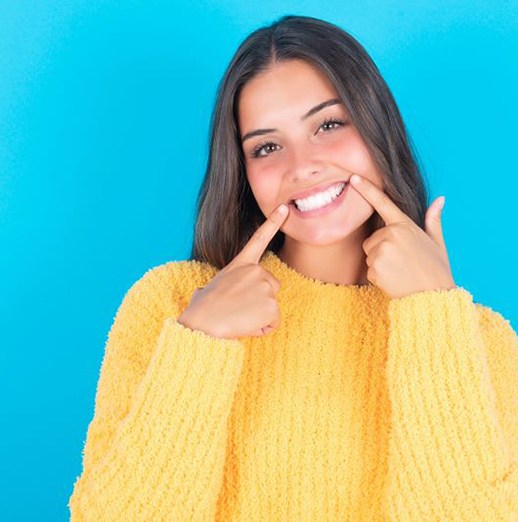 Woman in yellow sweater pointing at her healthy smile