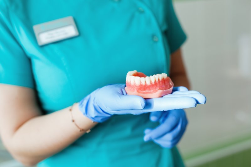 A young dentist holding a denture in her gloved hand